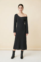 A woman wearing the long-sleeve Mantova Dress in black, featuring an asymmetrical off-the-shoulder neckline and vertical ribbed texture.