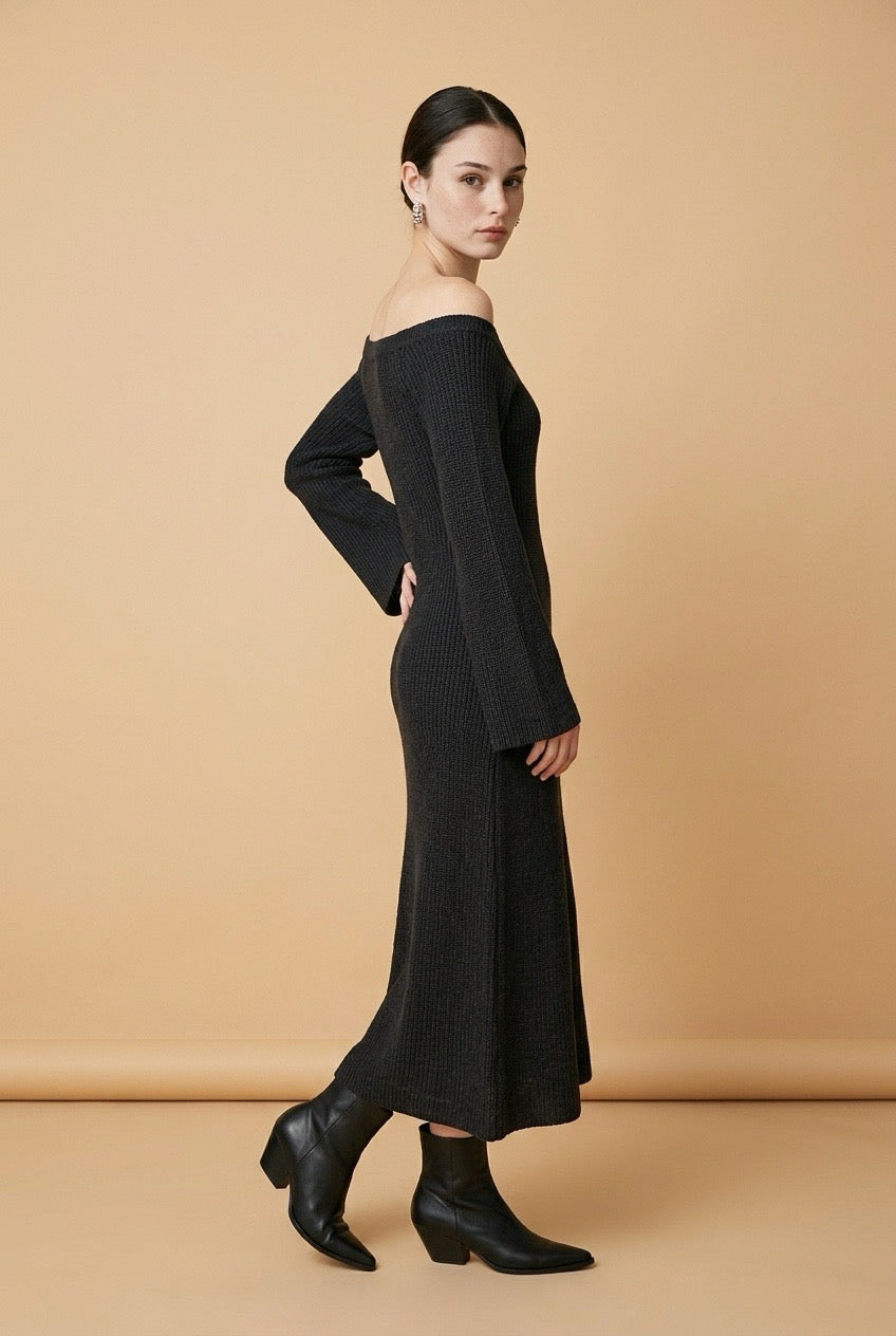 A woman wearing the long-sleeve Mantova Dress in black, featuring an asymmetrical off-the-shoulder neckline and vertical ribbed texture.