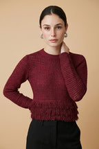 A woman wearing the Nerano long sleeve knit top in burgundy, featuring a crew neck, textured mesh stitch, and double-tiered fringe hem.