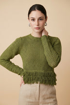 A woman wearing the Nerano long sleeve knit top in olive green, featuring a crew neck, textured mesh stitch, and double-tiered fringe hem.