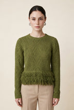 A woman wearing the Nerano long sleeve knit top in olive green, featuring a crew neck, textured mesh stitch, and double-tiered fringe hem.