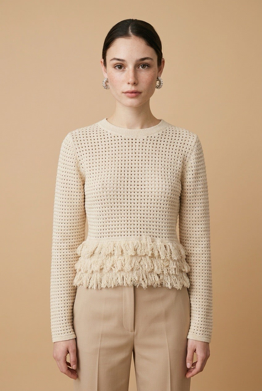 A woman wearing the Nerano long sleeve knit top in beige, featuring a crew neck, textured mesh stitch, and double-tiered fringe hem.