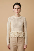 A woman wearing the Nerano long sleeve knit top in beige, featuring a crew neck, textured mesh stitch, and double-tiered fringe hem.