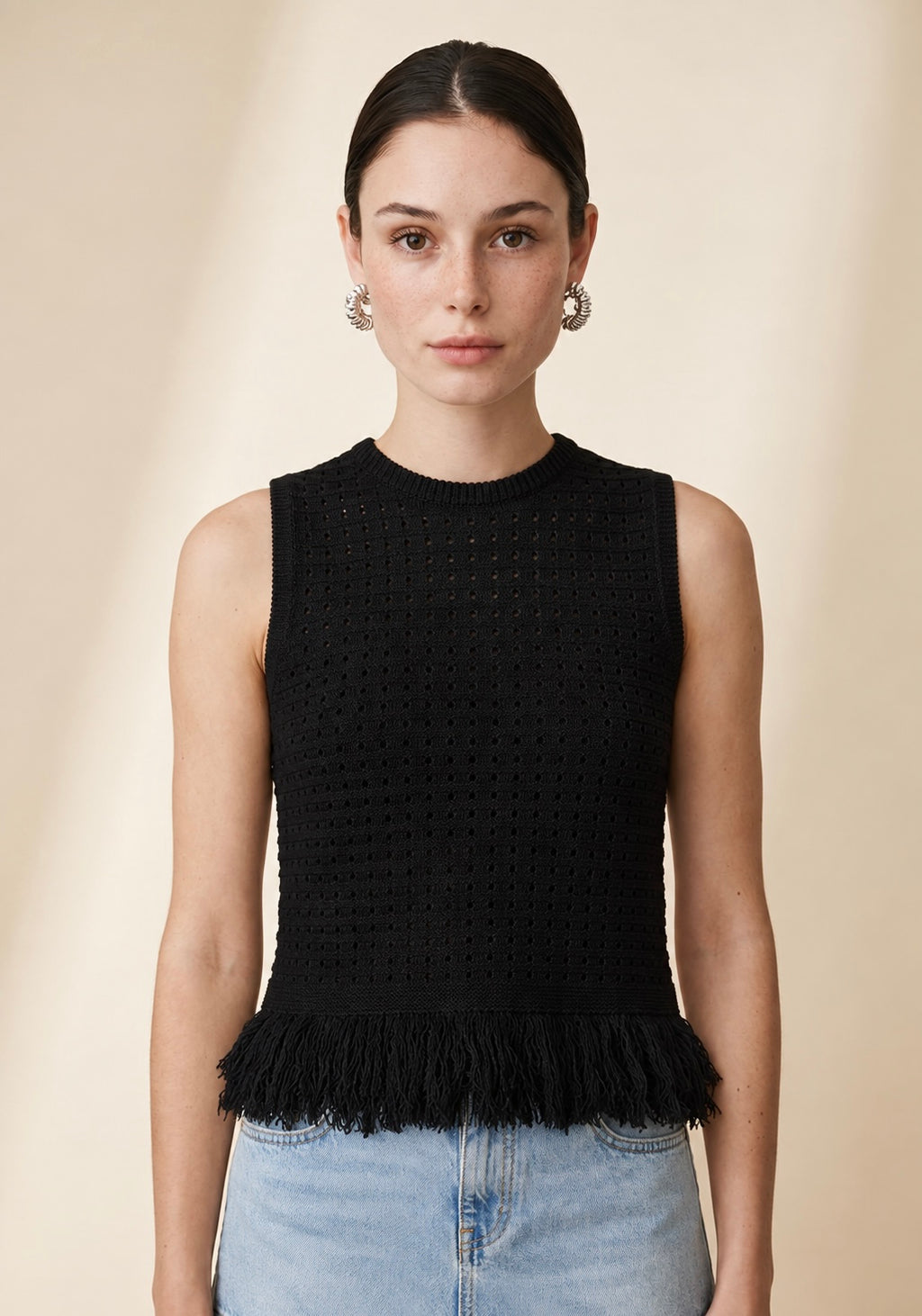 Model wearing the black Nerano sleeveless knit top with a crew neckline, textured eyelet pattern, and fringe hem trim