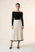 A woman wearing the Padova pleated knit midi skirt in off-white, highlighting its A-line flare and contrasting black hem line.