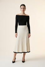 A woman wearing the Padova pleated knit midi skirt in off-white, highlighting its A-line flare and contrasting black hem line.