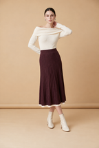 A woman wearing the Padova pleated knit midi skirt in burgundy, showcasing its vertical pleats and contrasting trim.
