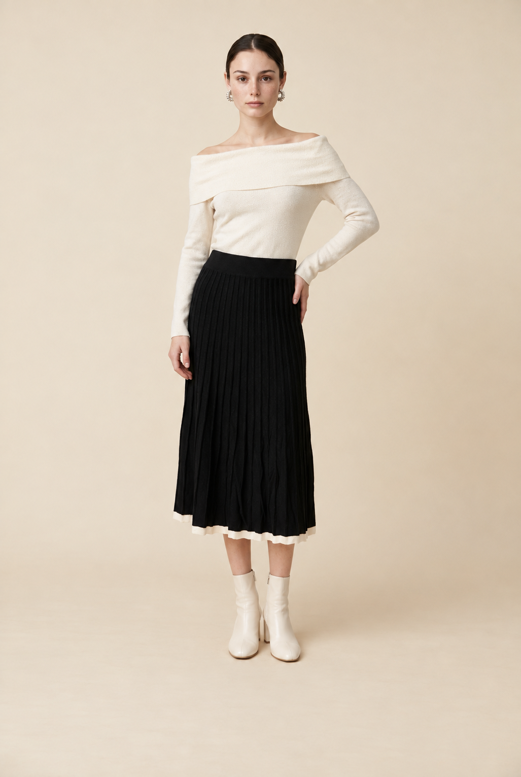 A woman wearing the Padova pleated knit midi skirt in black, featuring elegant vertical pleats and smooth drape.