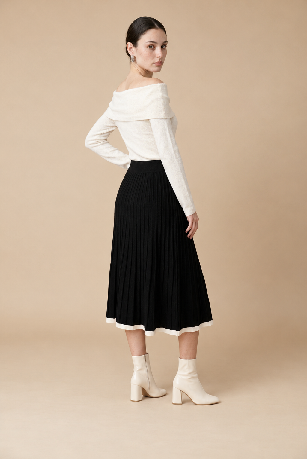A woman wearing the Padova pleated knit midi skirt in black, featuring elegant vertical pleats and smooth drape.