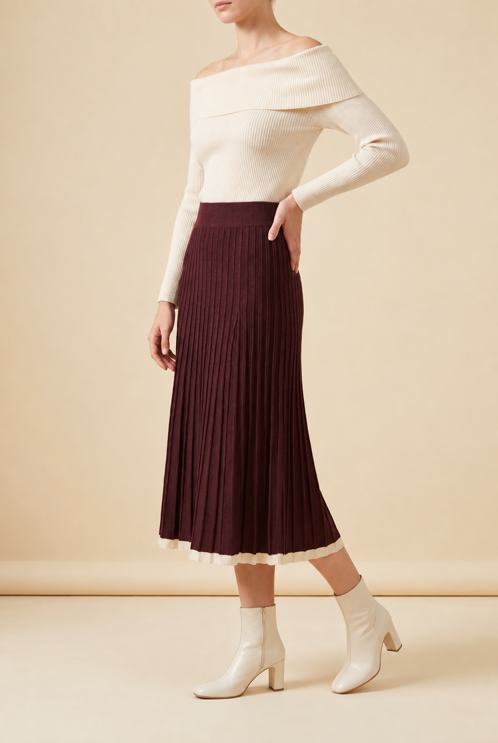 A woman wearing the Padova pleated knit midi skirt in burgundy, showcasing its vertical pleats and contrasting trim.