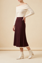 A woman wearing the Padova pleated knit midi skirt in burgundy, showcasing its vertical pleats and contrasting trim.