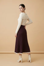 A woman wearing the Padova pleated knit midi skirt in burgundy, showcasing its vertical pleats and contrasting trim.
