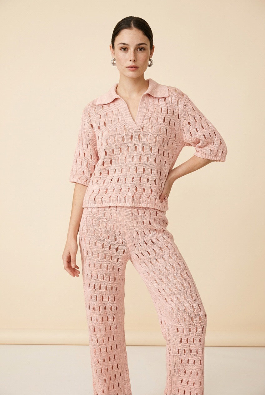 A woman wearing the Set Positano open-knit two-piece set in light pink, featuring a collared polo top and matching wide-leg trousers.
