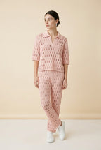 A woman wearing the Set Positano open-knit two-piece set in light pink, featuring a collared polo top and matching wide-leg trousers.