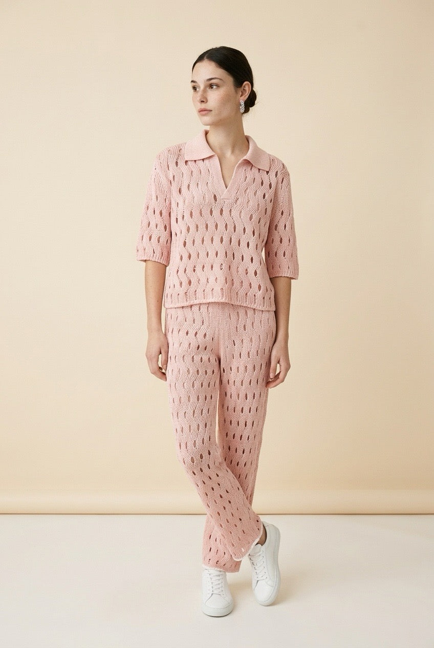 A woman wearing the Set Positano open-knit two-piece set in light pink, featuring a collared polo top and matching wide-leg trousers.
