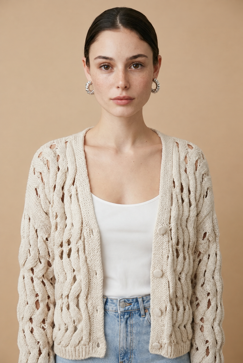 A woman wearing the Taormina open-knit cardigan in neutral beige, featuring a button-down front and relaxed fit.