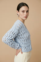 A woman wearing the Taormina open-knit cardigan in baby blue, featuring a button-down front and relaxed fit.