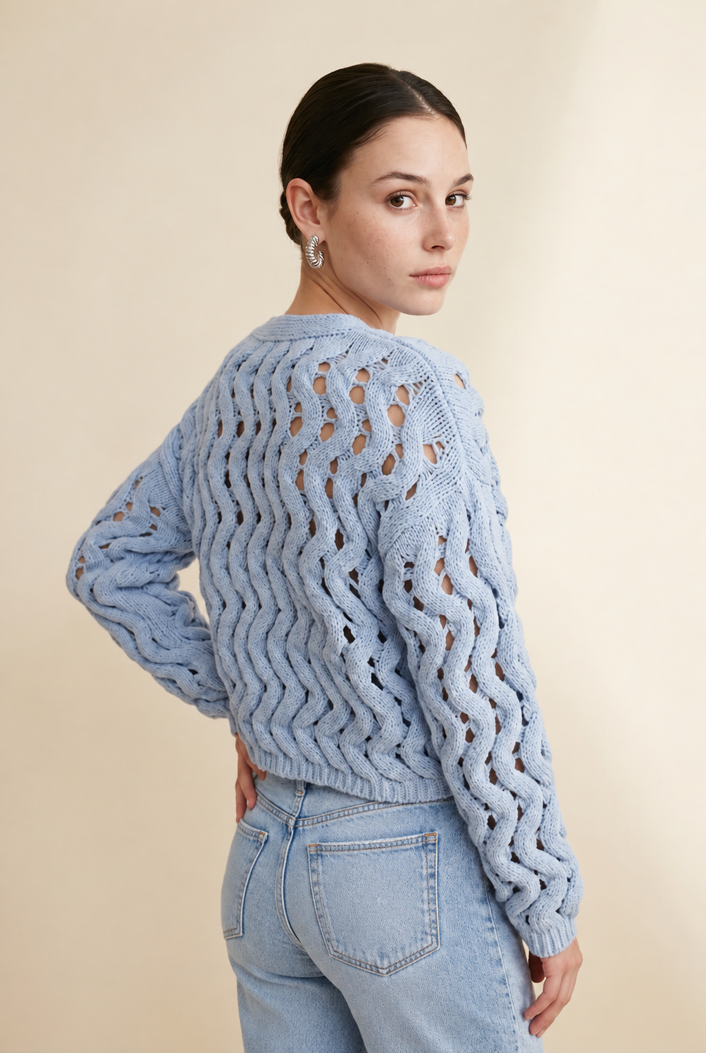 A woman wearing the Taormina open-knit cardigan in baby blue, featuring a button-down front and relaxed fit.