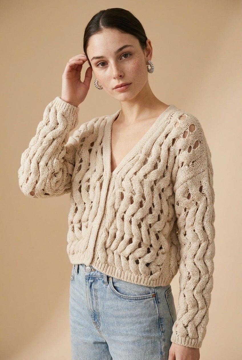 A woman wearing the Taormina open-knit cardigan in neutral beige, featuring a button-down front and relaxed fit.