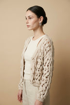A woman wearing the Taormina open-knit cardigan in neutral beige, featuring a button-down front and relaxed fit.