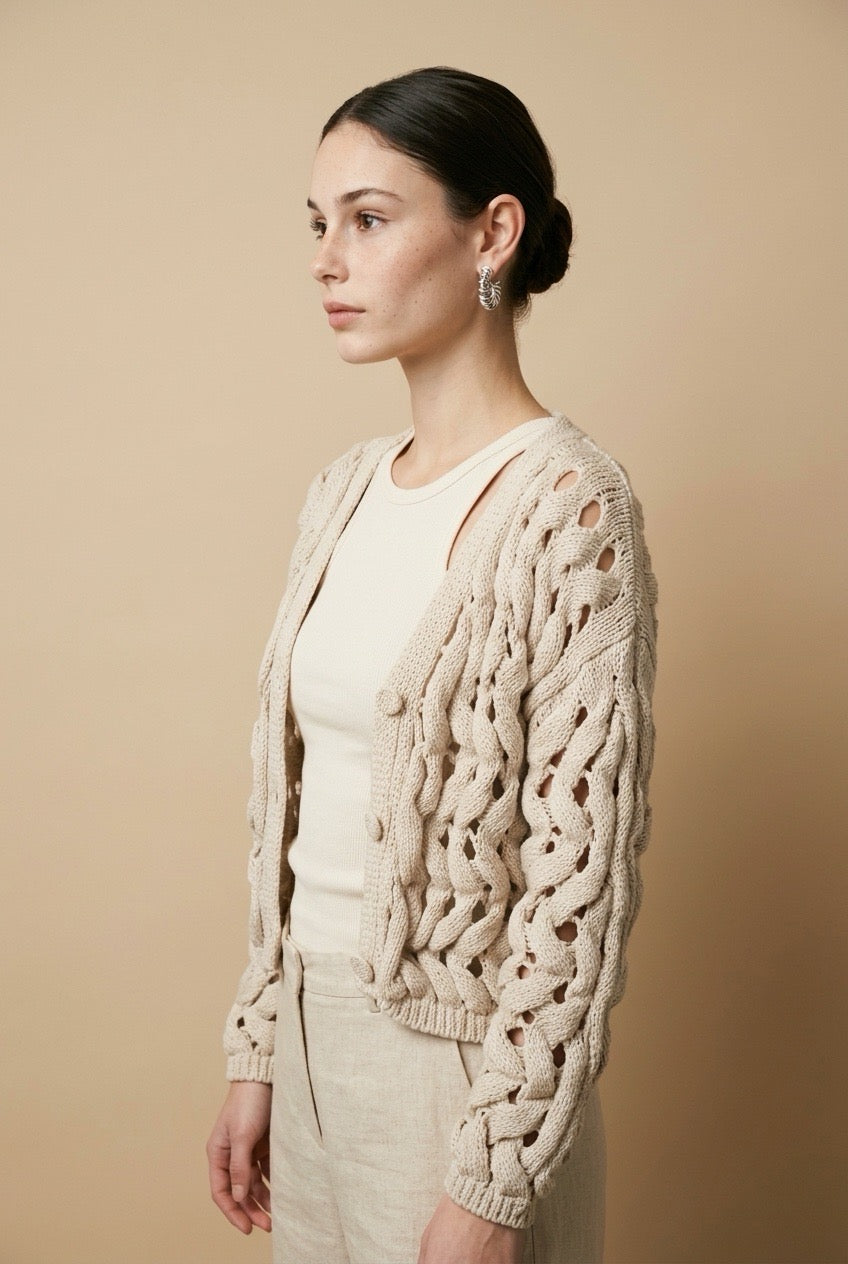 A woman wearing the Taormina open-knit cardigan in neutral beige, featuring a button-down front and relaxed fit.